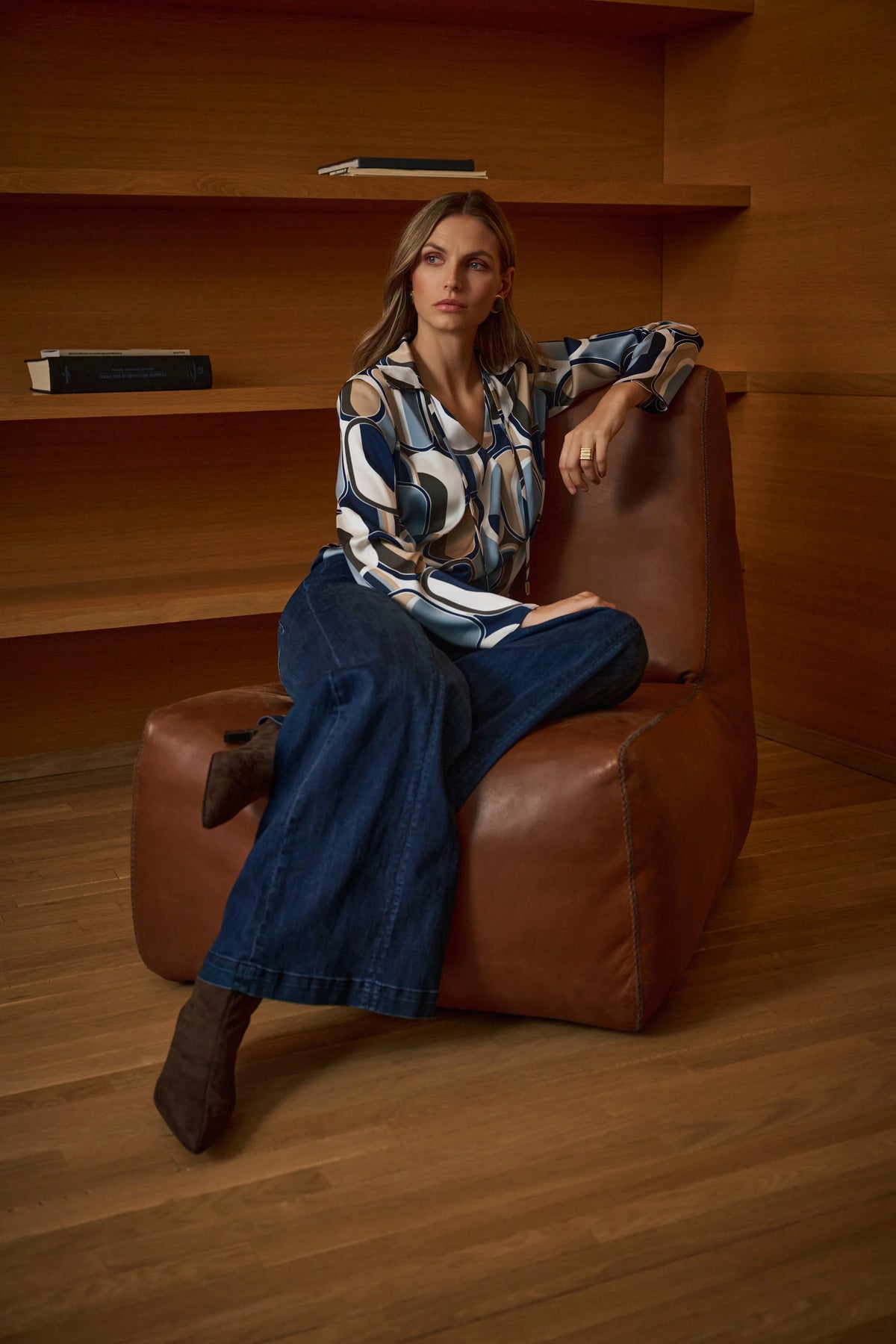 Woman sitting on a brown leather chair in a wooden room. Joseph Ribkoff Featherweave Palazzo High-Rise Jeans in Dark Denim Blue, style 263901 