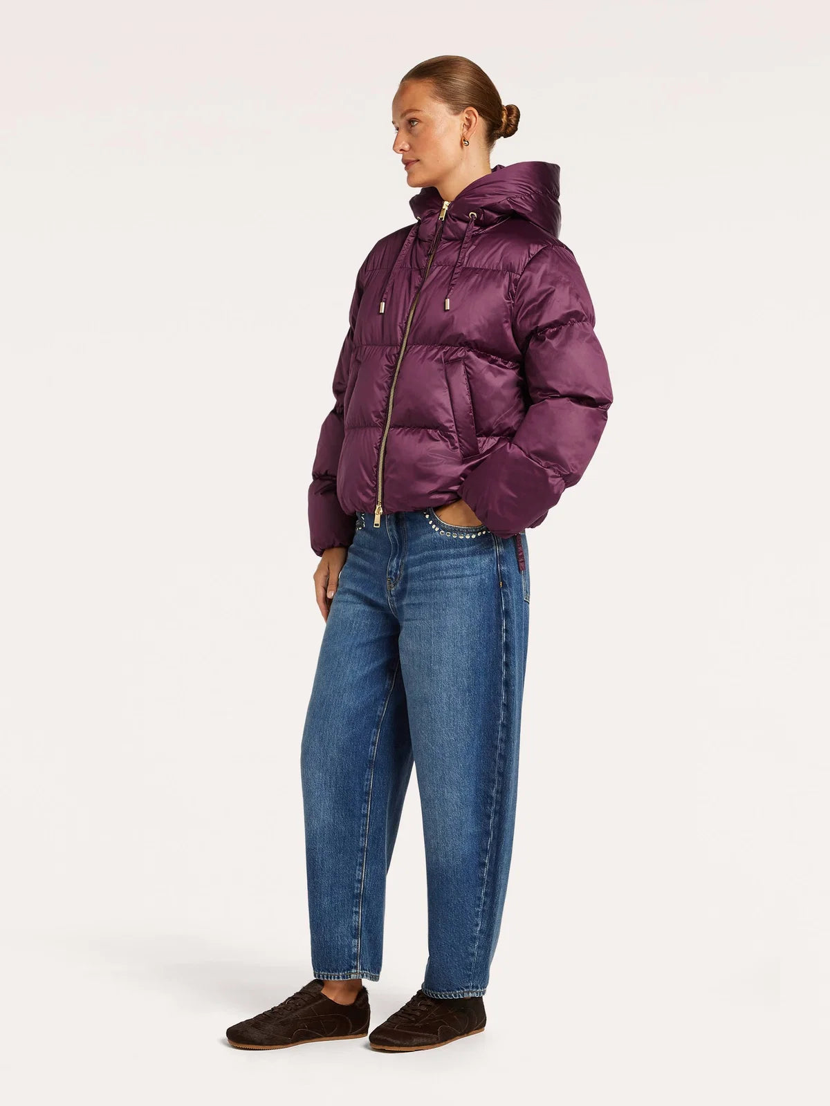A woman modeling a beaumont marian jacket dark berry , paired with blue jeans and dark brown shoes, standing against a plain off-white studio background.