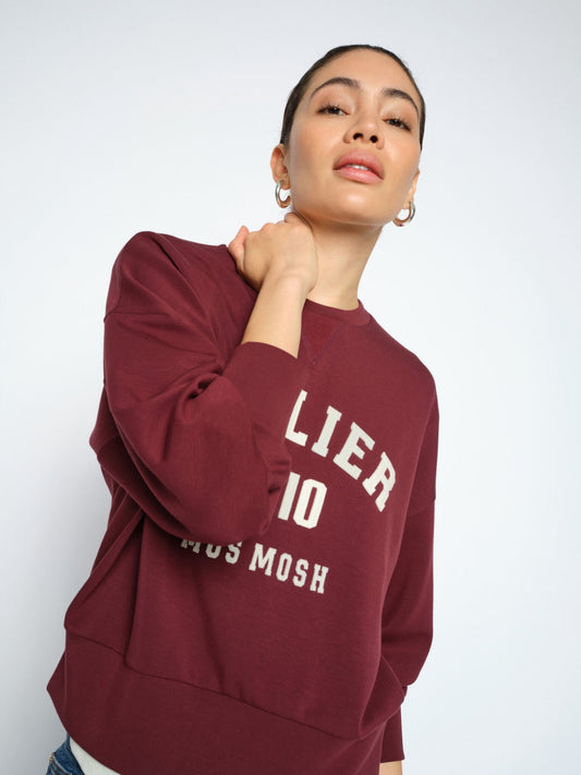 A woman wearing mosmosh mmnima sweatshirt 177510nport royale ' on the front, posed against a light gray studio background.